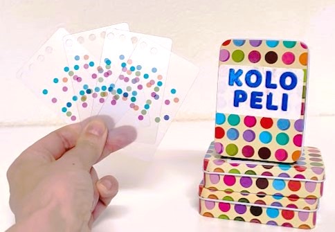 Metallinen kolopeli rasia, sekä käsi, jossa on erilaisia kortteja