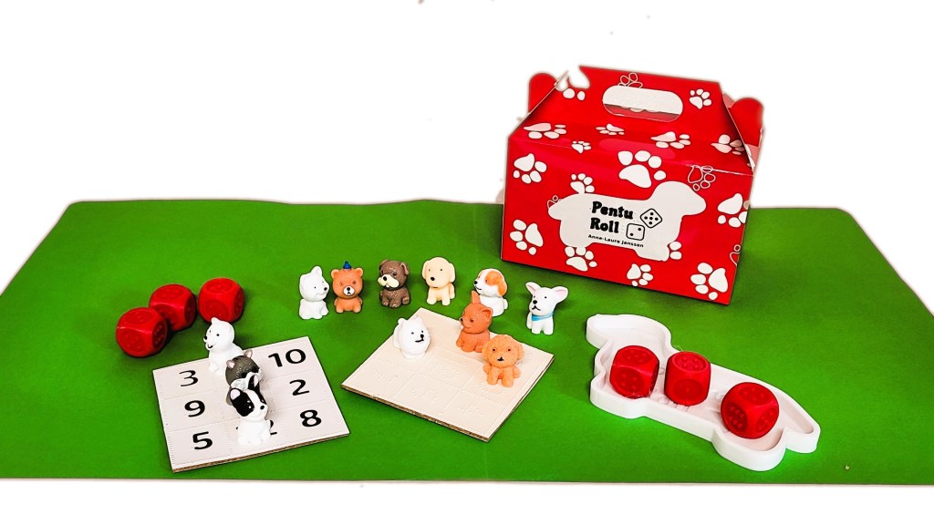 Penturoll peli: punainen laatikko, jossa on tassumerkkejä, erilaisia pieniä koirahahmoja, taktiilinoppeja sekä par ruudukkoa. Yhdellä on teksti painettuna ja pistekirjoituksella, toisella on tekti kohotekstinä